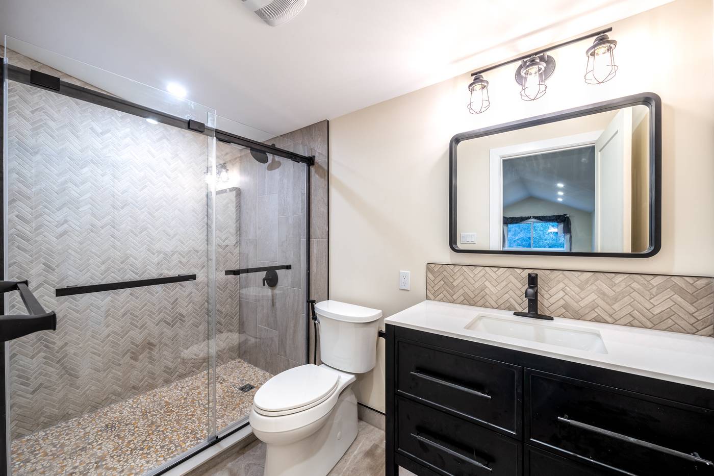 Taupe Herringbone Bathroom Retreat, Whitby: Bathroom with a sliding-door shower, black vanity and herringbone backsplash