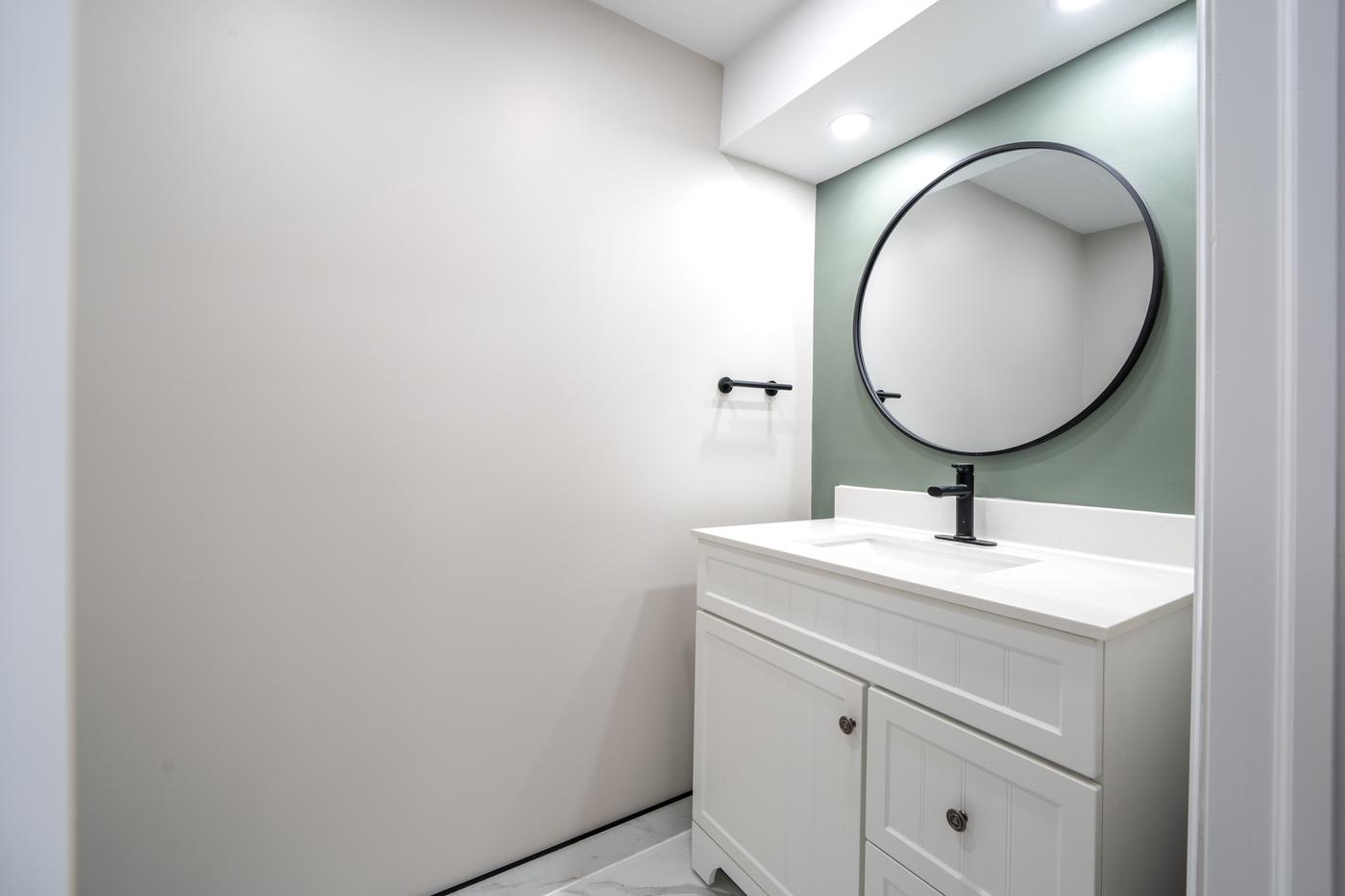 Open-Concept Basement Suite, Oshawa: Powder room vanity with a round mirror and green accent wall