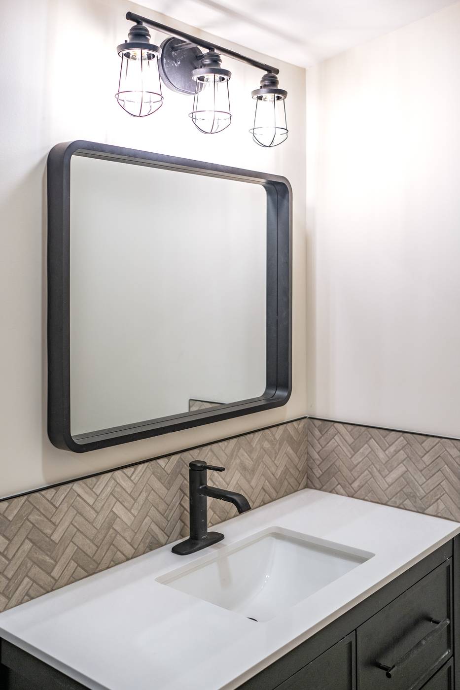 Taupe Herringbone Bathroom Retreat, Whitby: Rounded black mirror with industrial vanity lights over the sink