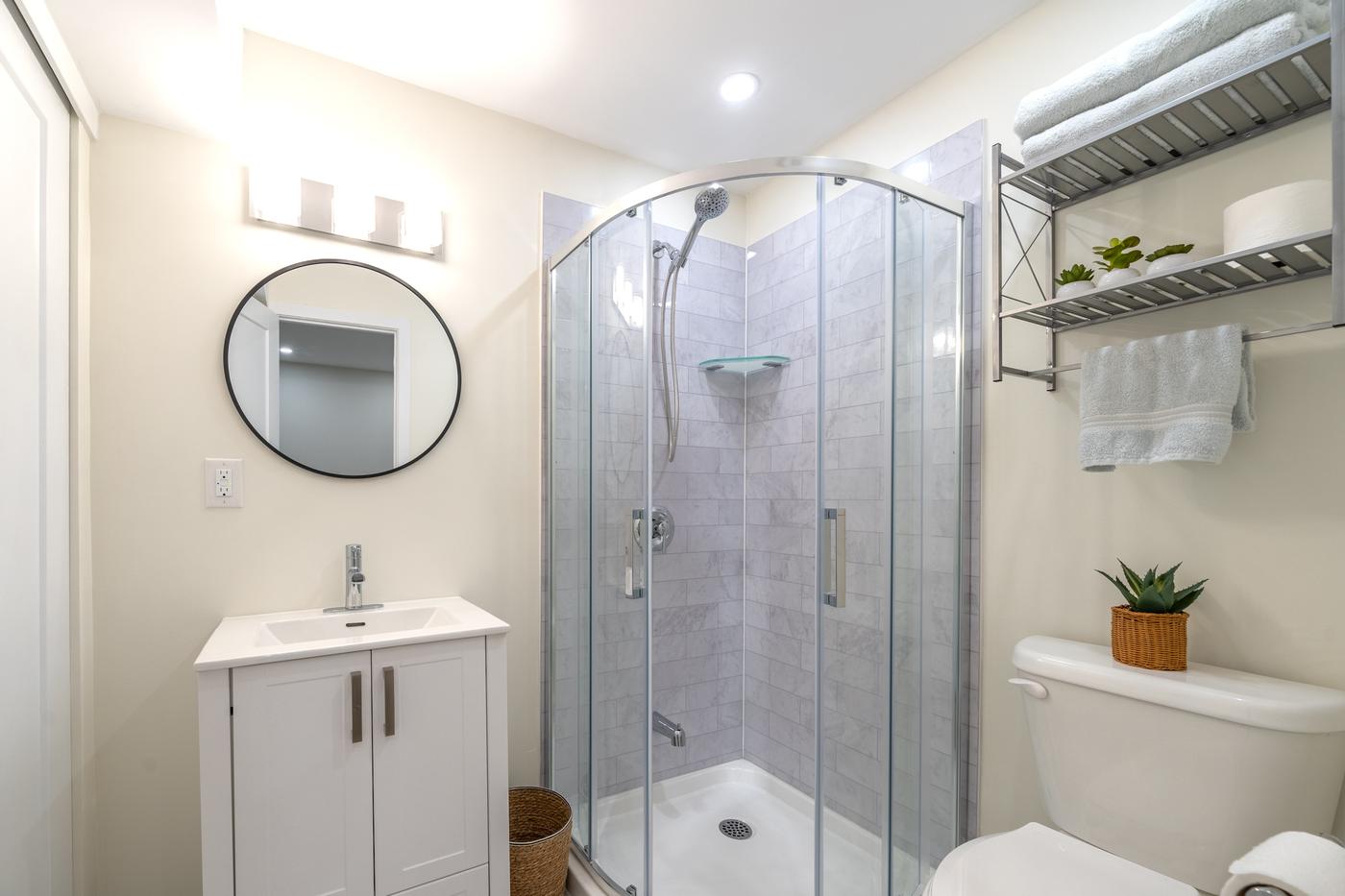 Stone Fireplace Basement Retreat, Oshawa: Basement bathroom with a corner glass shower and round mirror