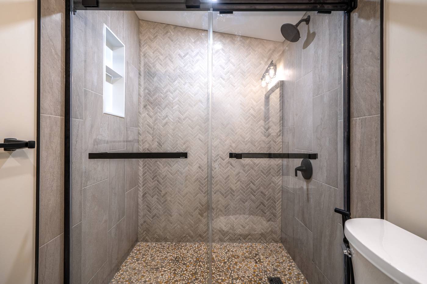 Taupe Herringbone Bathroom Retreat, Whitby: Sliding glass shower with a herringbone wall, niche and pebble floor