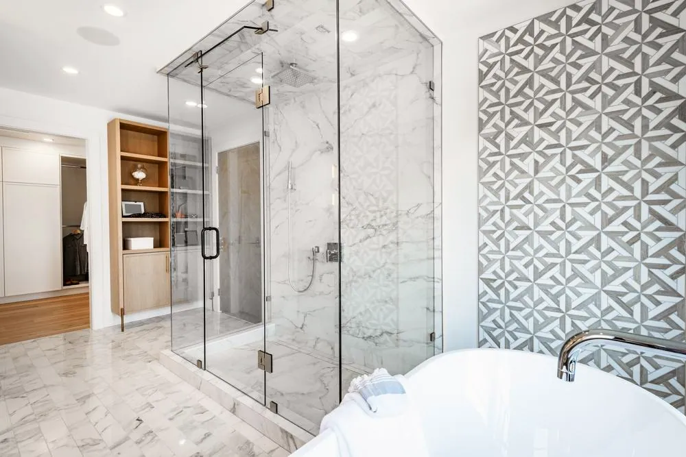 Bathroom with a frameless glass shower, marble-look tile, freestanding tub and a patterned feature wall