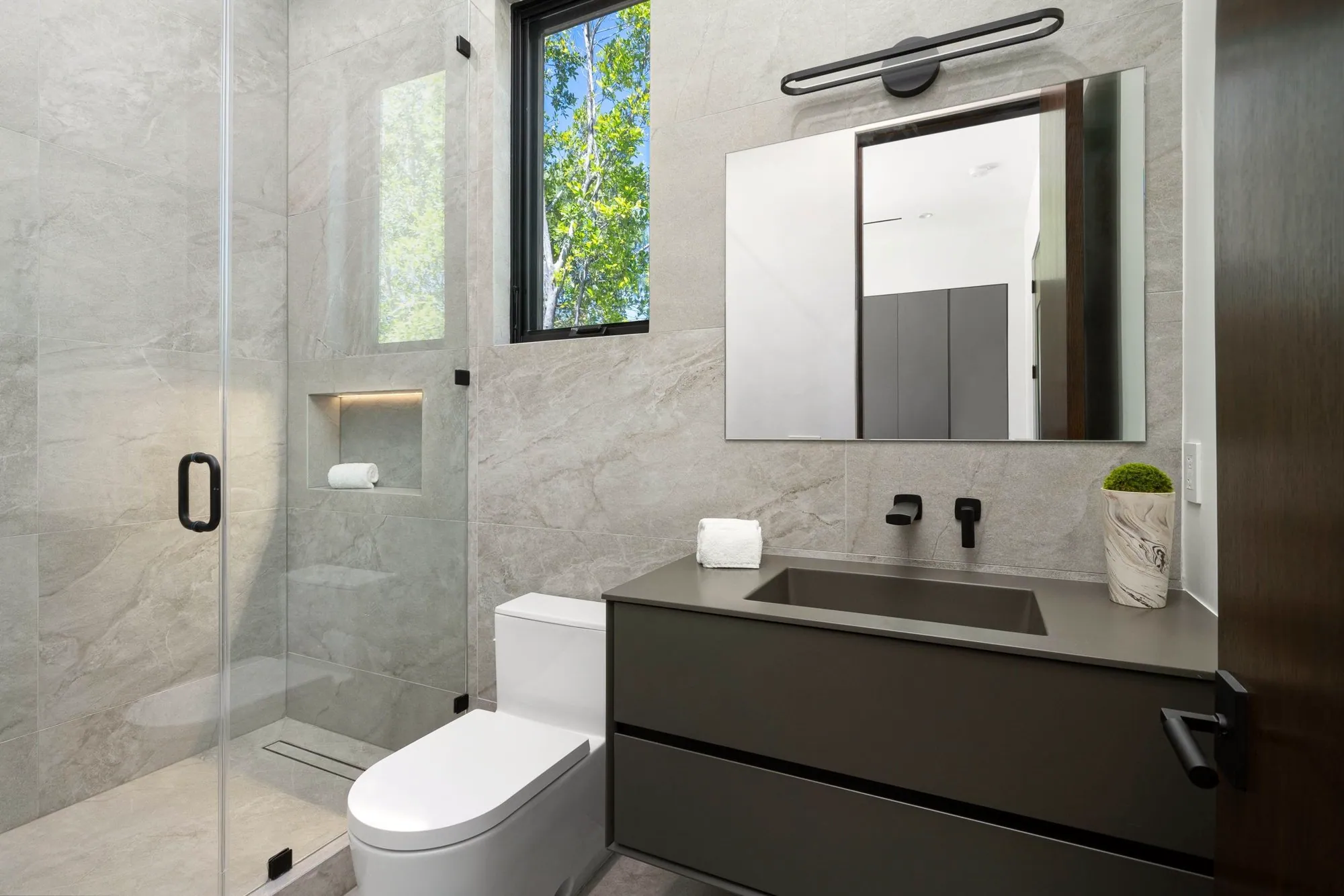 Bathroom with large stone-look porcelain tile, a lit shower niche and a floating dark vanity