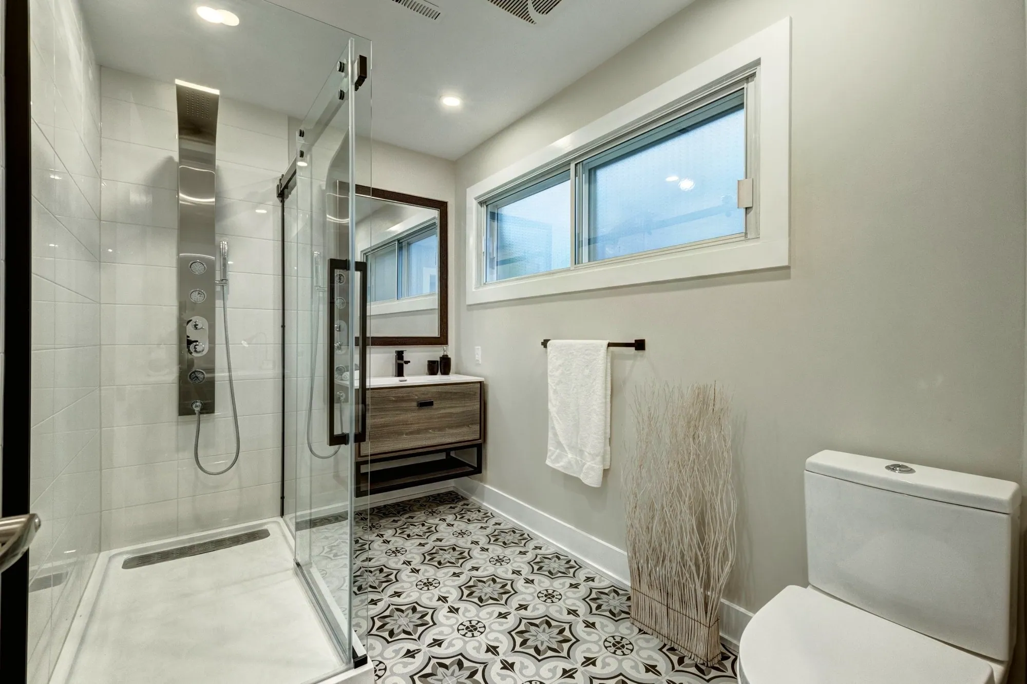 Bathroom with patterned encaustic-look floor tile, a glass shower with a shower panel and a floating vanity