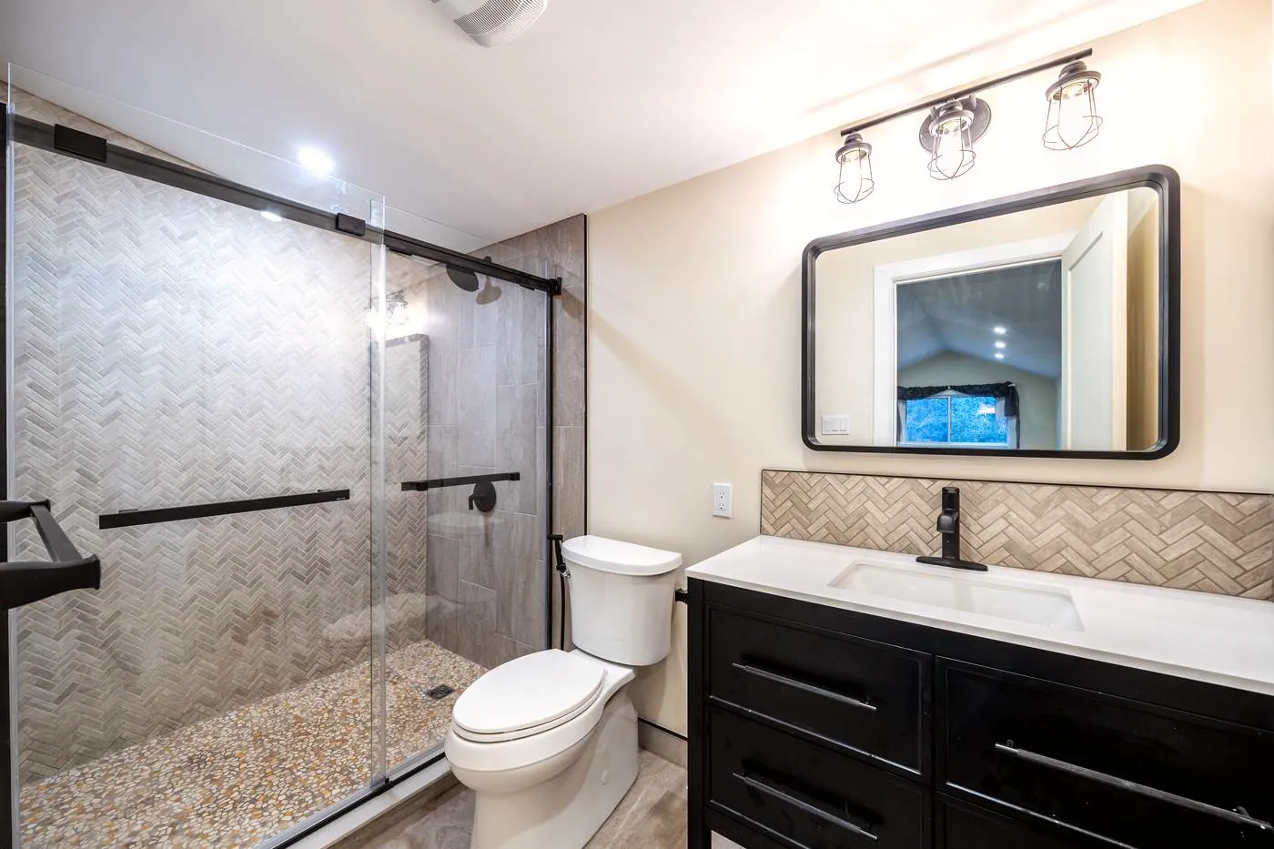 Taupe Herringbone Bathroom Retreat: Sliding-door shower, black vanity and herringbone backsplash