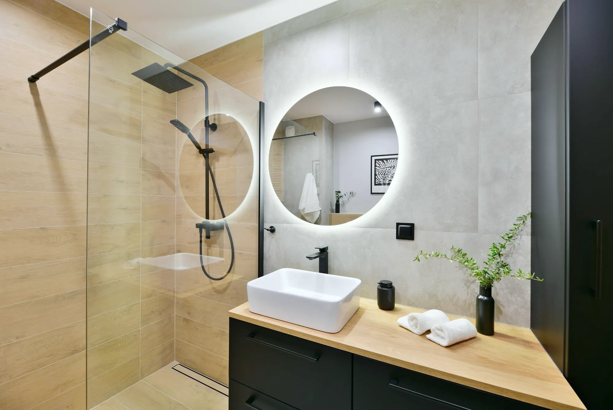 Bathroom with wood-look shower tile, a walk-in glass shower, round backlit mirror and vessel sink