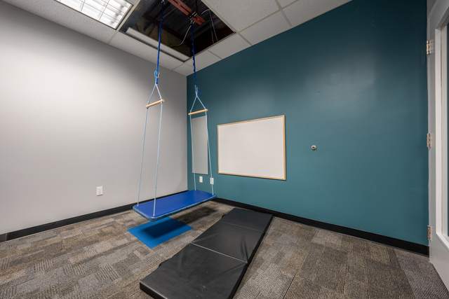 Dots for Kids Occupational Therapy Centre, Whitby: Therapy room with a teal accent wall, whiteboard and hanging swing bench