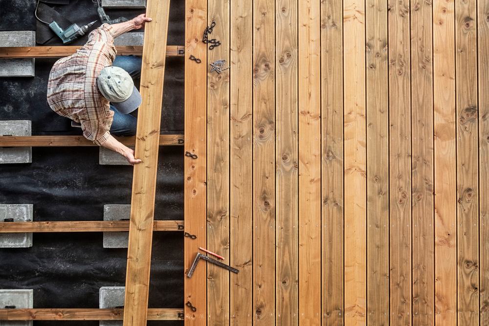 Carpenter laying deck boards over a joist frame