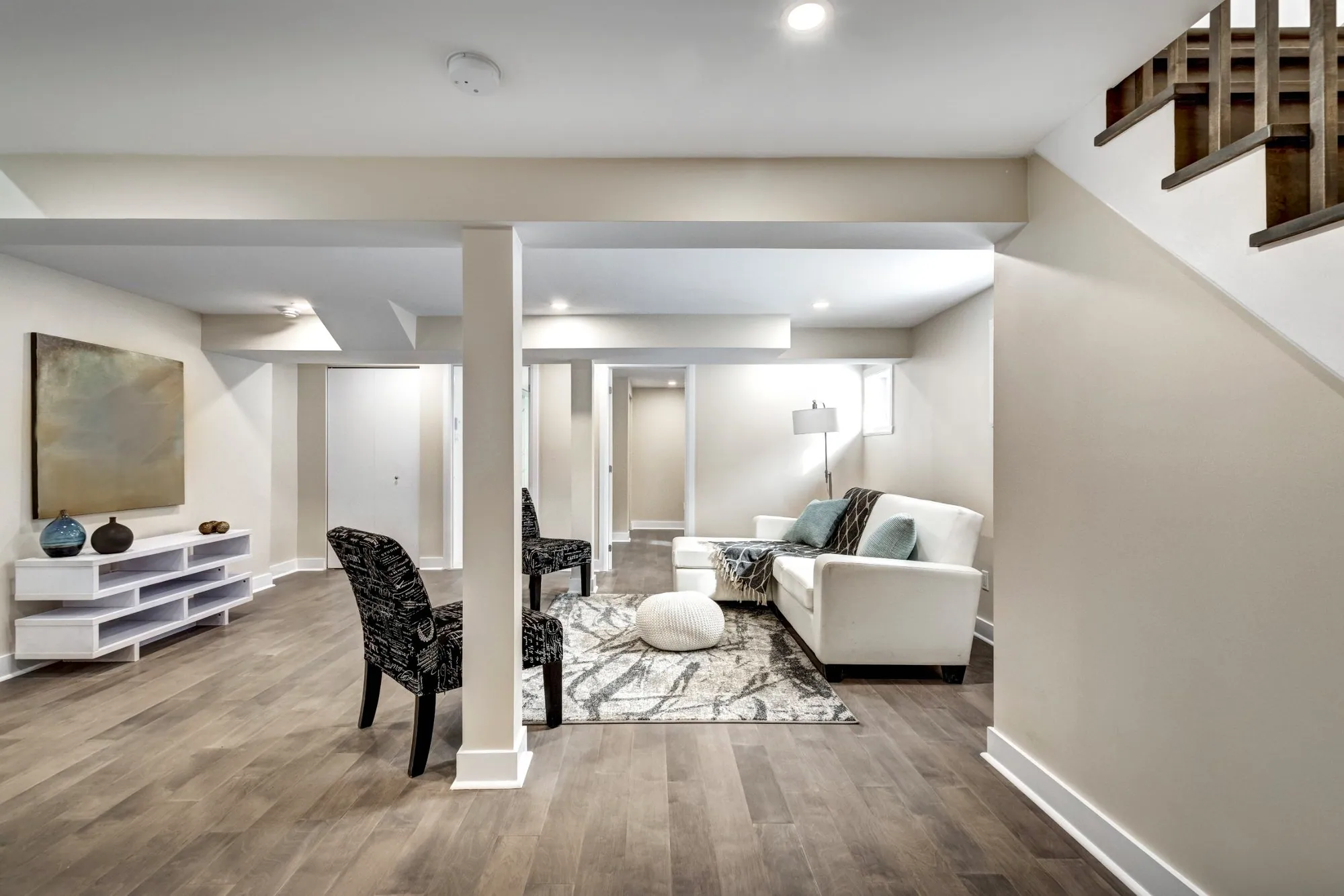 Finished basement living area with a wrapped support column, bulkheads, pot lights and plank flooring