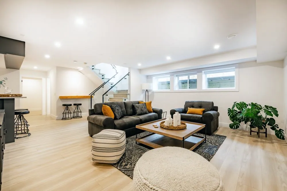 Finished basement living room with wood-look flooring, a glass-railed staircase and a kitchenette