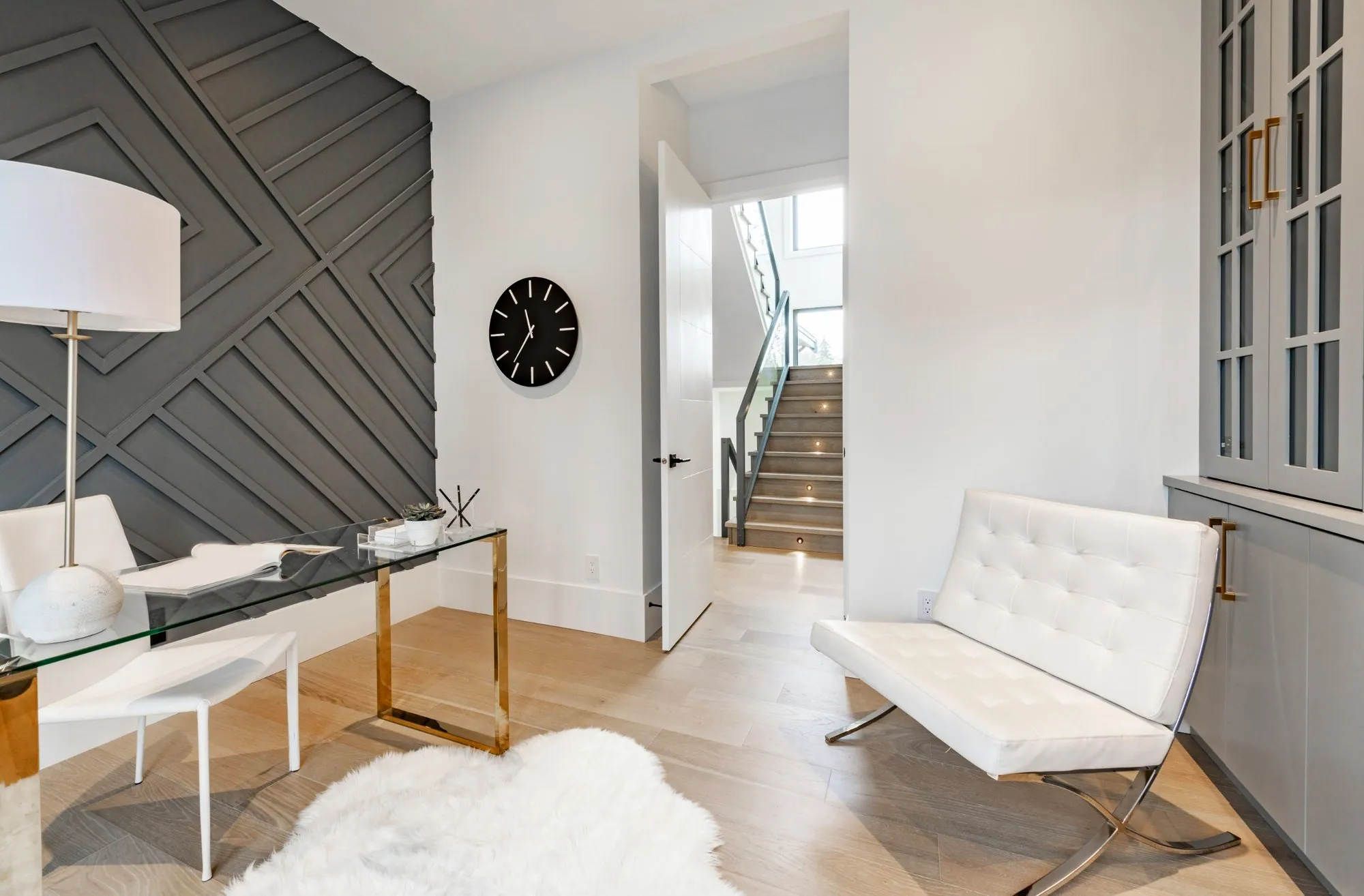 Home office with a grey geometric wood-panel accent wall, glass desk and built-in cabinets