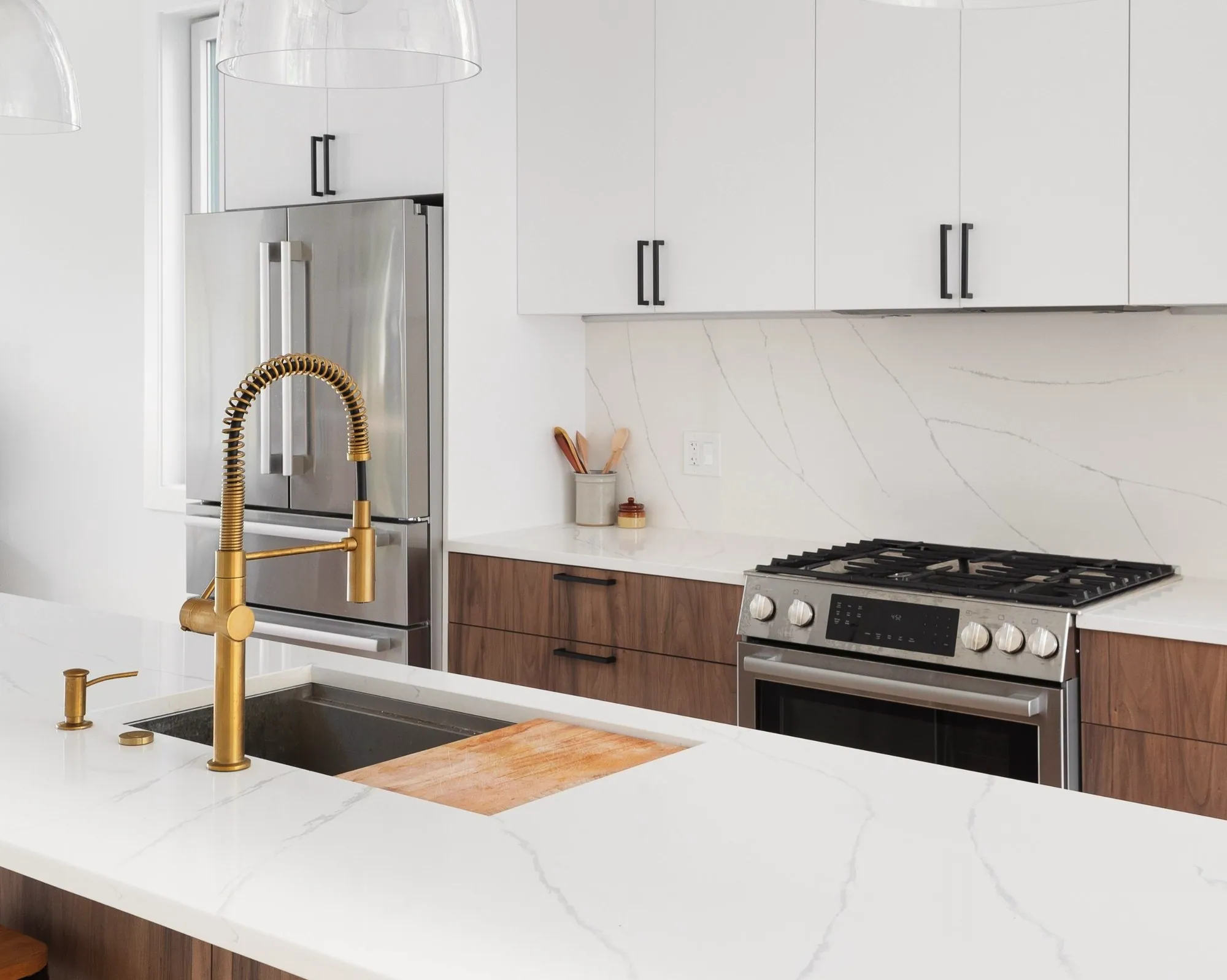 Kitchen with a brass spring faucet, walnut lower cabinets, white quartz slab backsplash and gas range