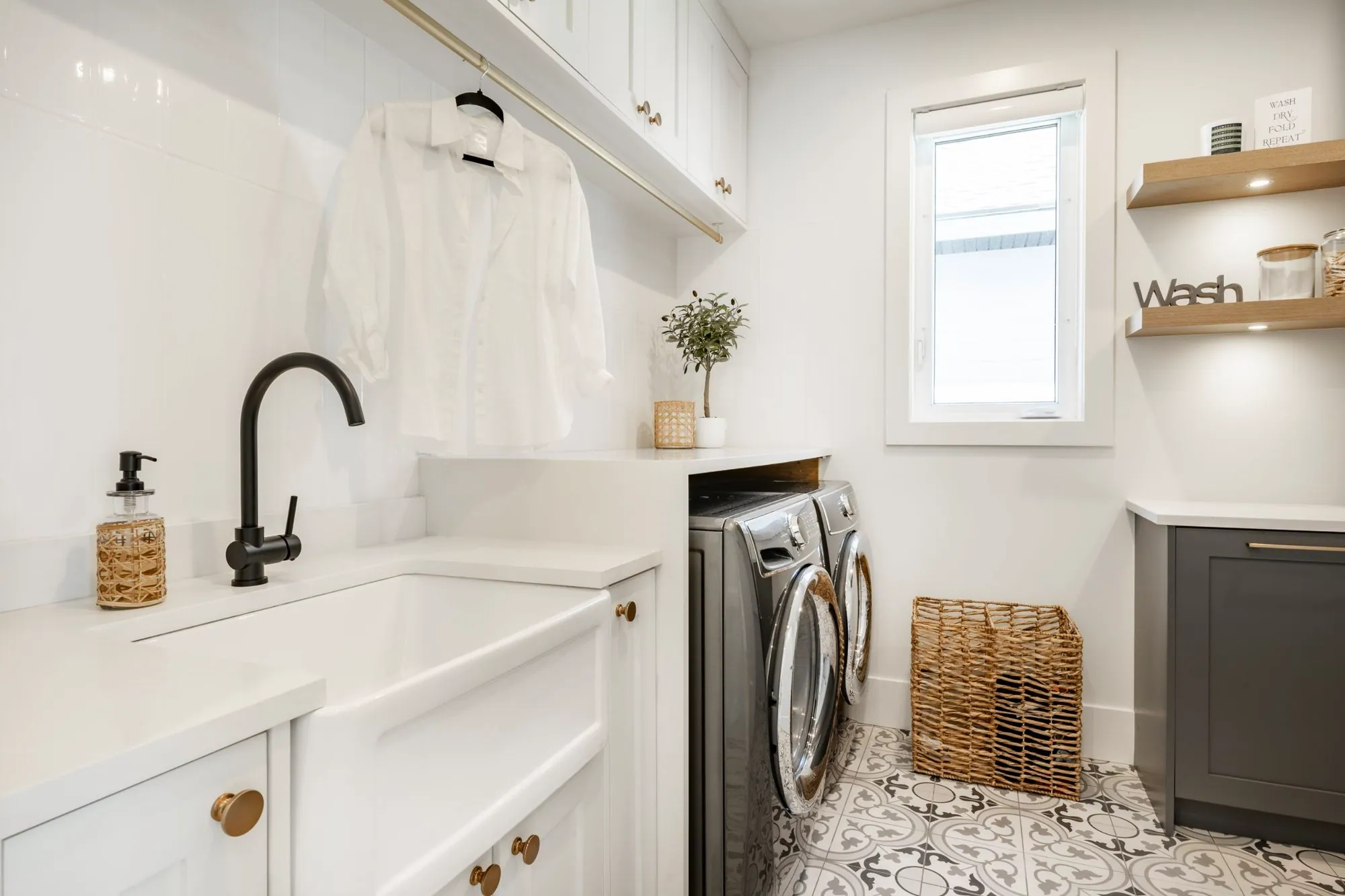 Laundry room with a white farmhouse sink, black faucet, front-load washer and dryer and patterned floor tile