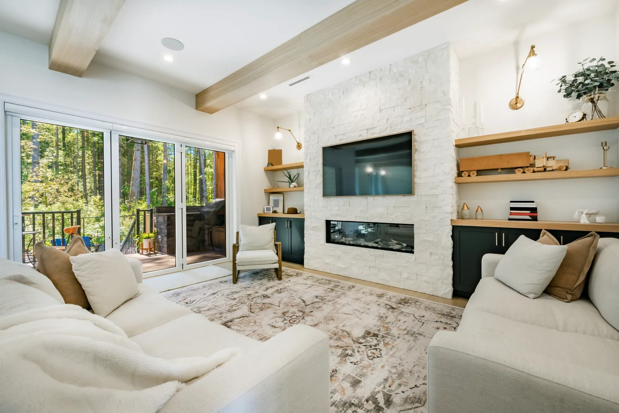 Living room with a white stacked stone fireplace, floating oak shelves and folding doors to a deck