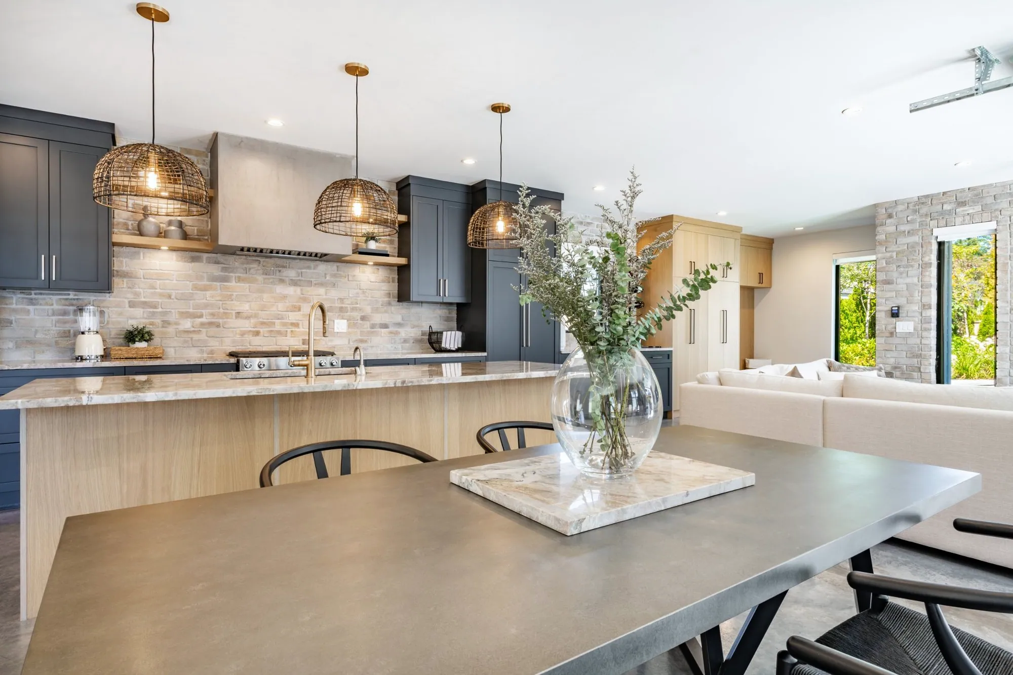 Navy shaker kitchen with a whitewashed brick backsplash, open oak shelves and woven pendants over a long island