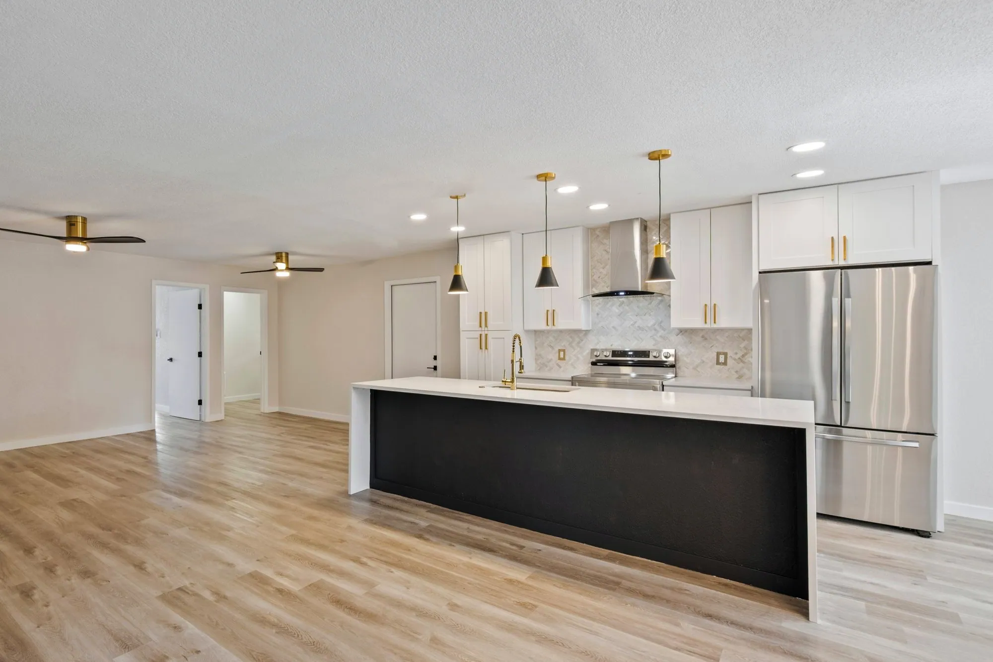 Open-concept kitchen with a long black waterfall island, gold pendants and wood-look vinyl plank flooring