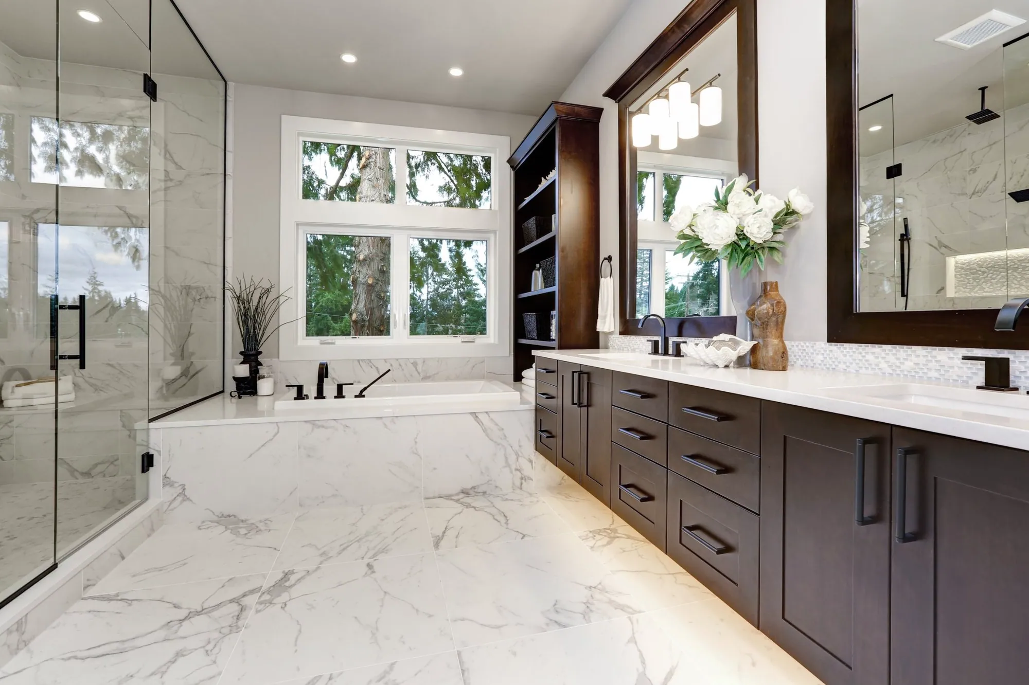 Primary bathroom with marble-look porcelain floors, a tiled tub deck, a glass shower and a dark wood double vanity