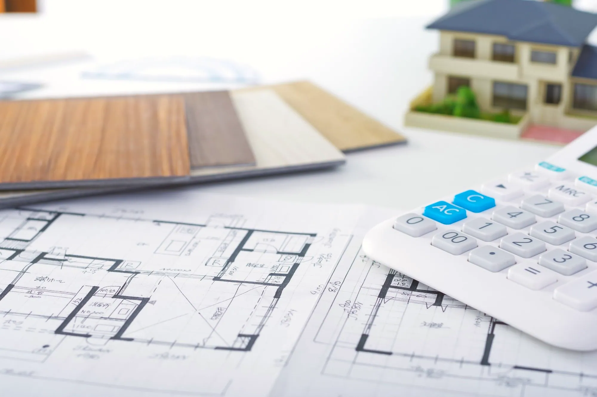 Renovation floor plans, flooring samples, a calculator and a model house on a desk