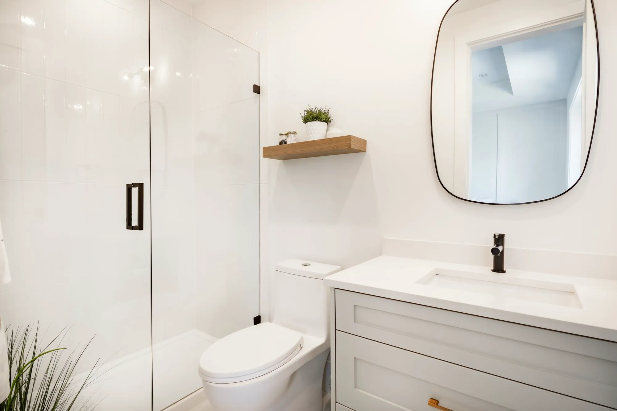 Small white bathroom with a frameless glass shower, floating oak shelf and grey shaker vanity