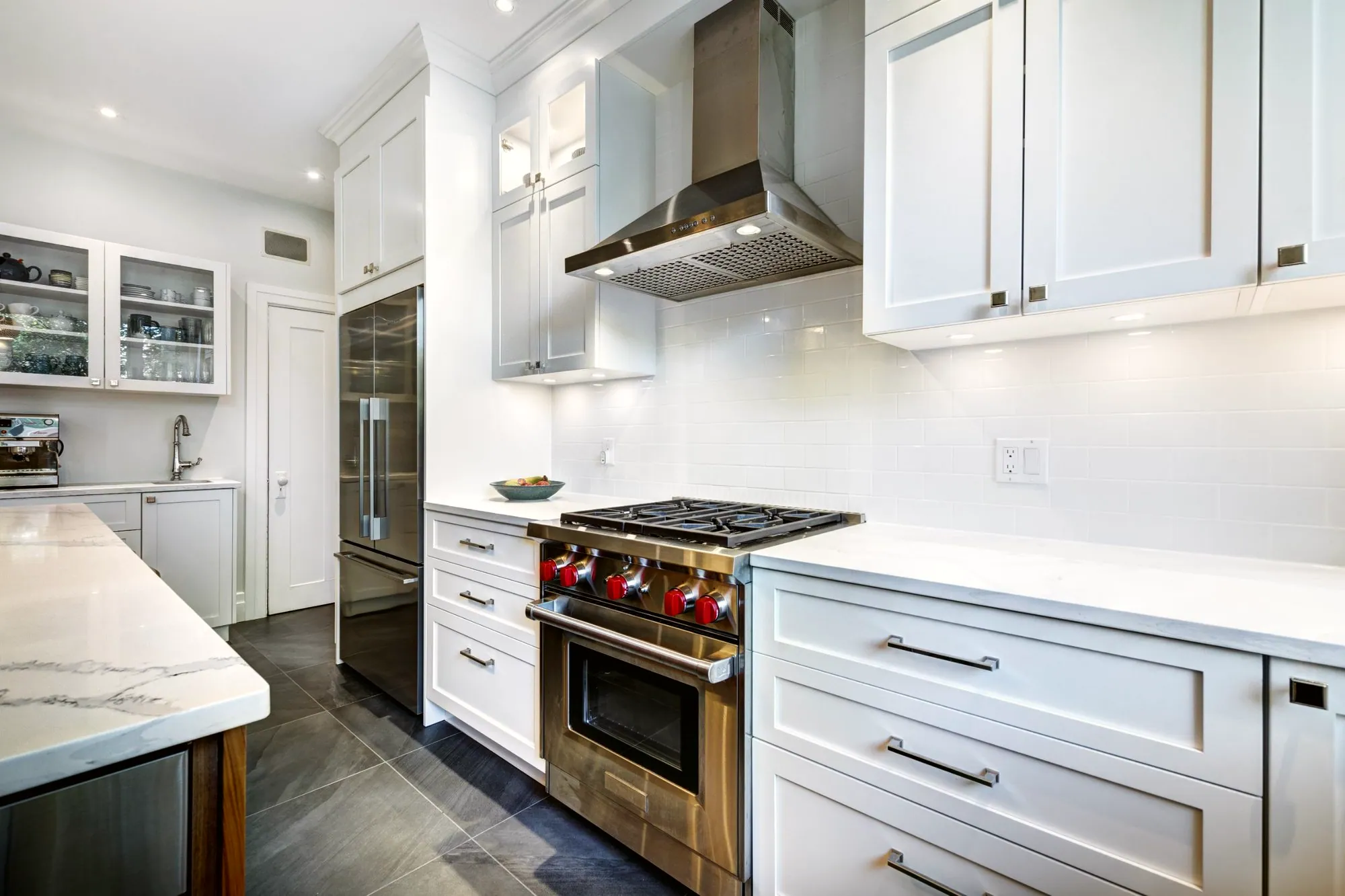 Stainless range hood over white subway tile, white shaker cabinets and a professional gas range