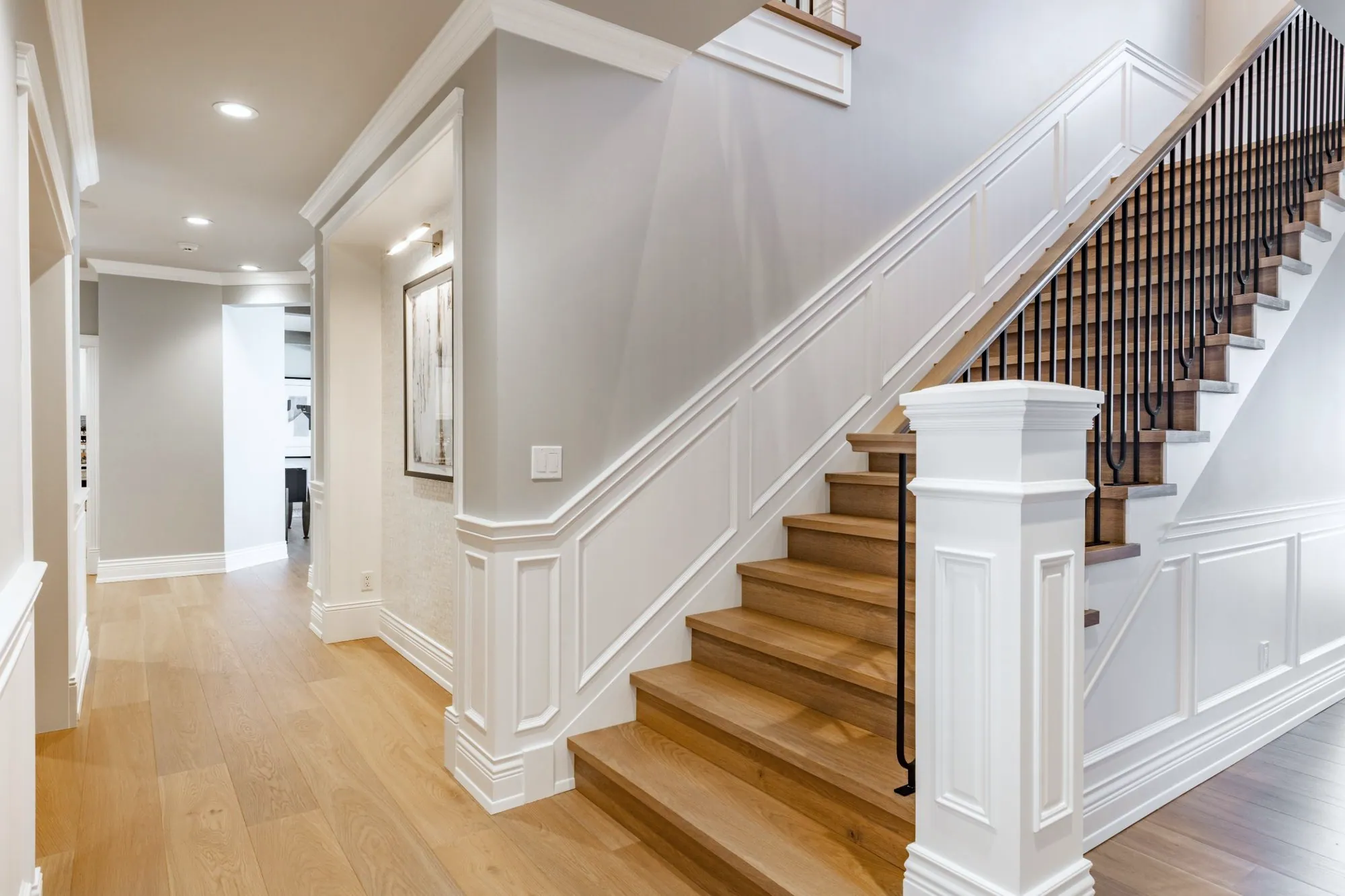 Staircase with oak treads, white risers, black metal spindles and panelled wainscoting along the wall