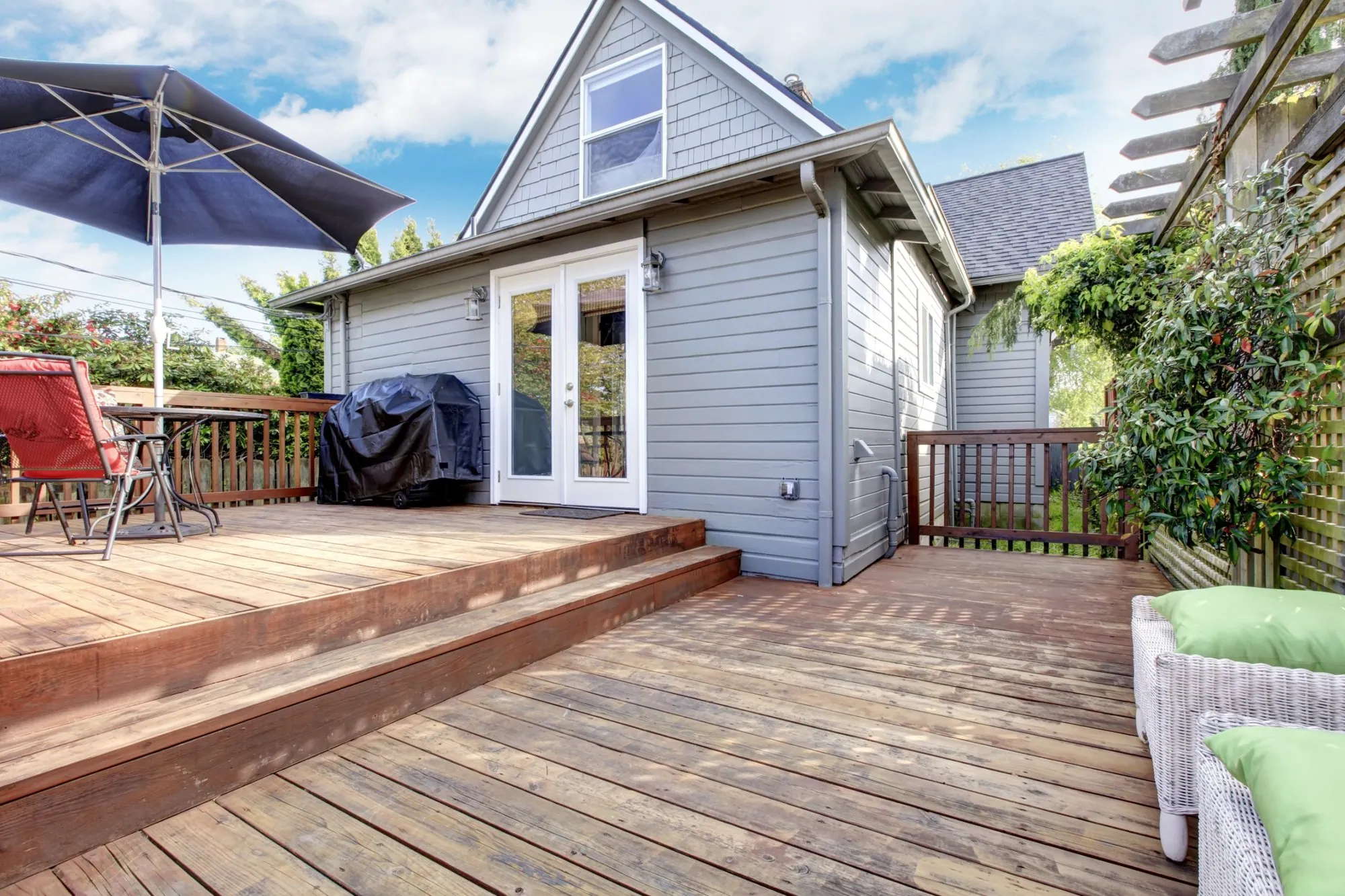 Two-level wood deck with wide steps, a patio umbrella and a barbecue behind a grey-sided house