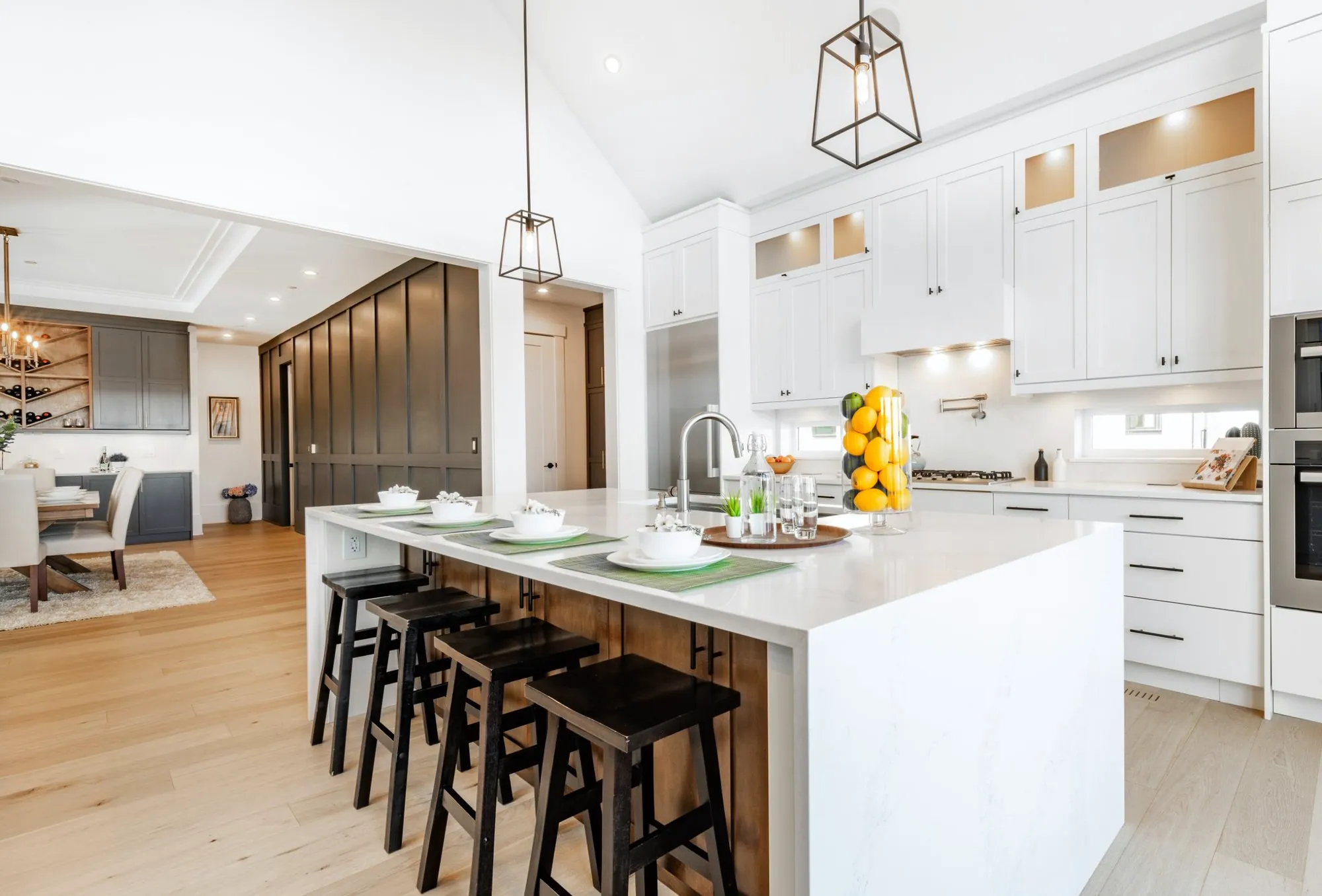 Vaulted white kitchen with a waterfall quartz island, black pendants and a wood-clad island base