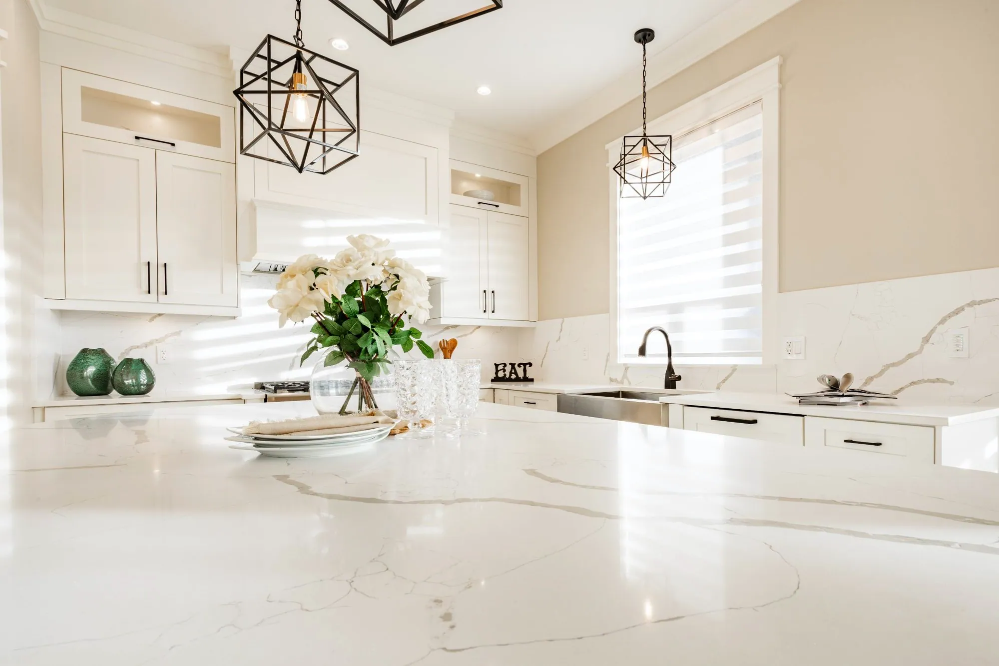 Veined white quartz kitchen island with geometric pendants and a full-height quartz backsplash