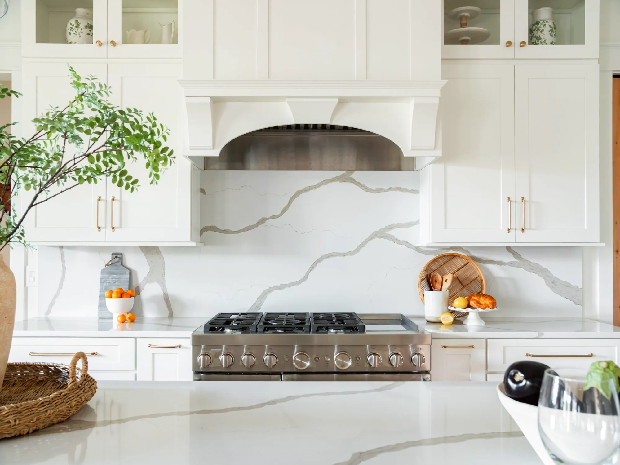 White kitchen with a full-height quartz slab backsplash, arched range hood and brass pulls