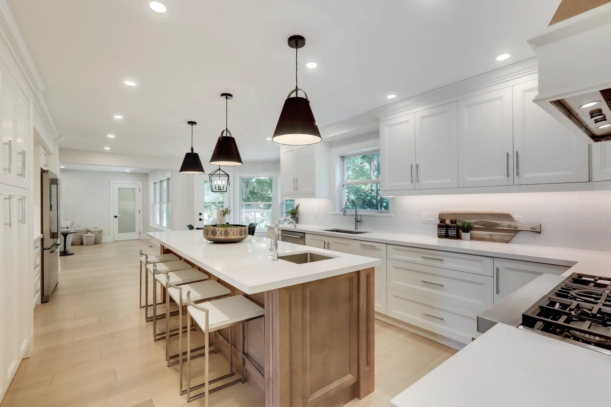 White kitchen with a long natural wood island, quartz counters and black cone pendants