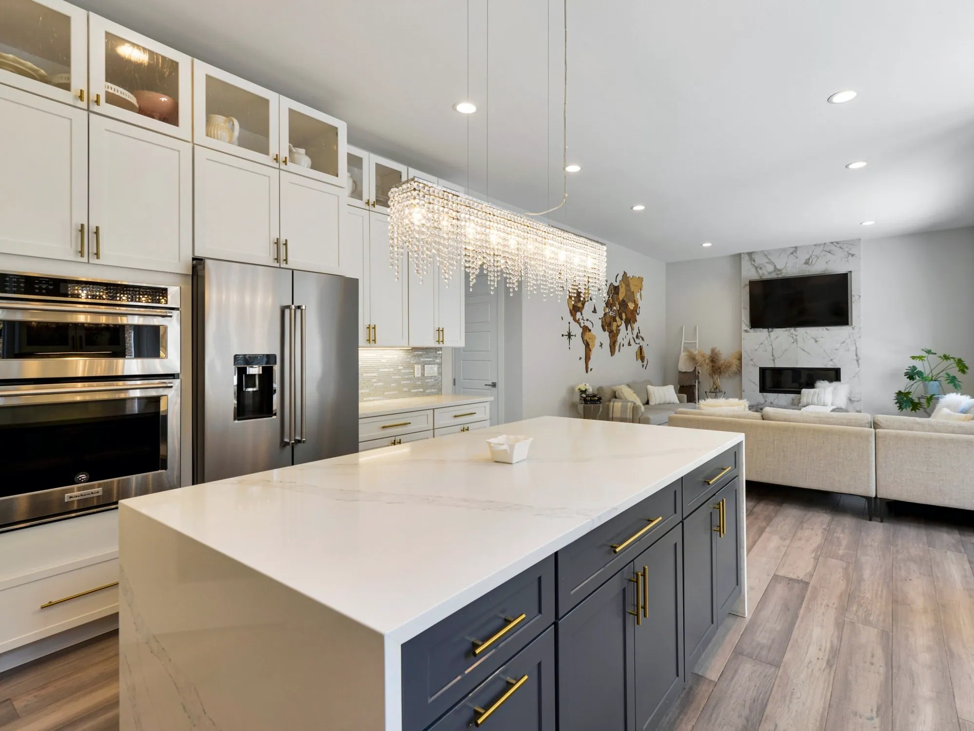 White kitchen with a navy island, gold pulls, waterfall quartz top and a crystal chandelier
