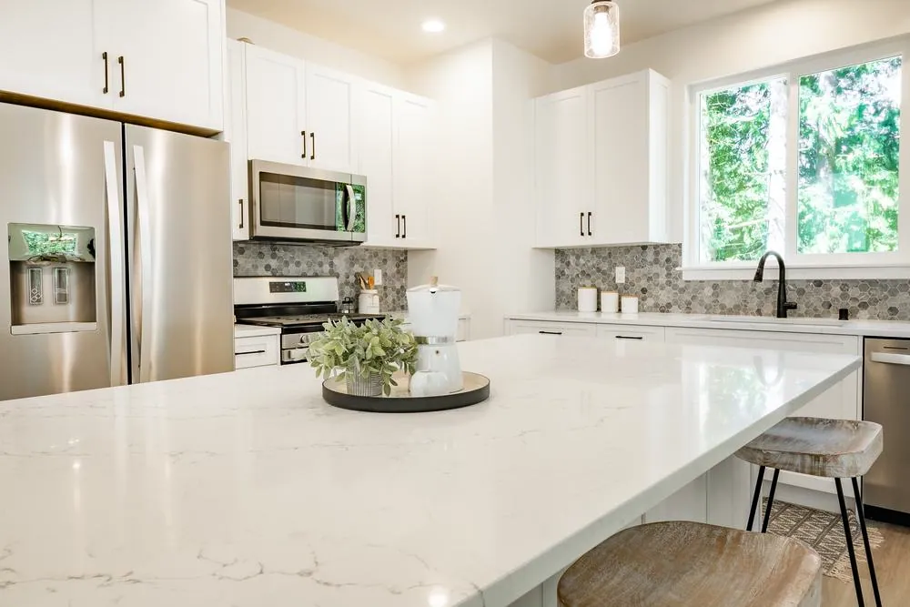 White kitchen with a quartz island, stainless appliances and a geometric tile backsplash