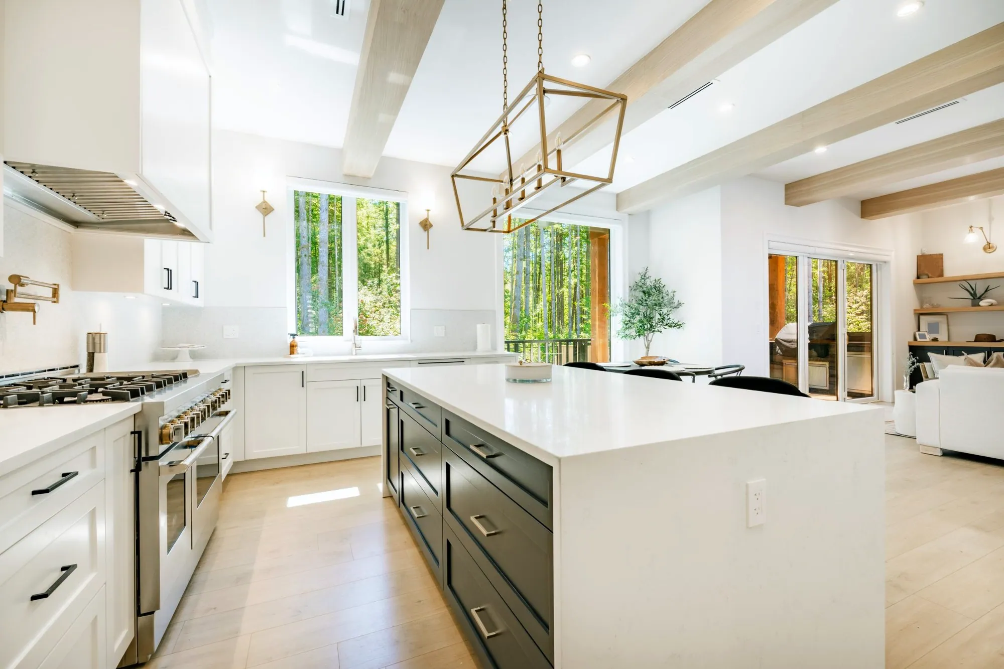 White kitchen with a waterfall quartz island, dark lower cabinets, wood ceiling beams and a gold lantern pendant