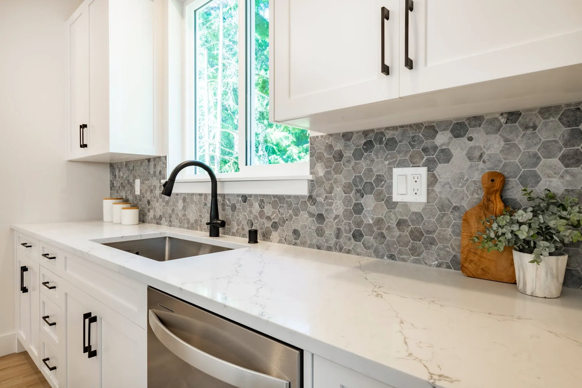 White shaker cabinets with a grey marble hexagon mosaic backsplash, quartz counters and a black faucet