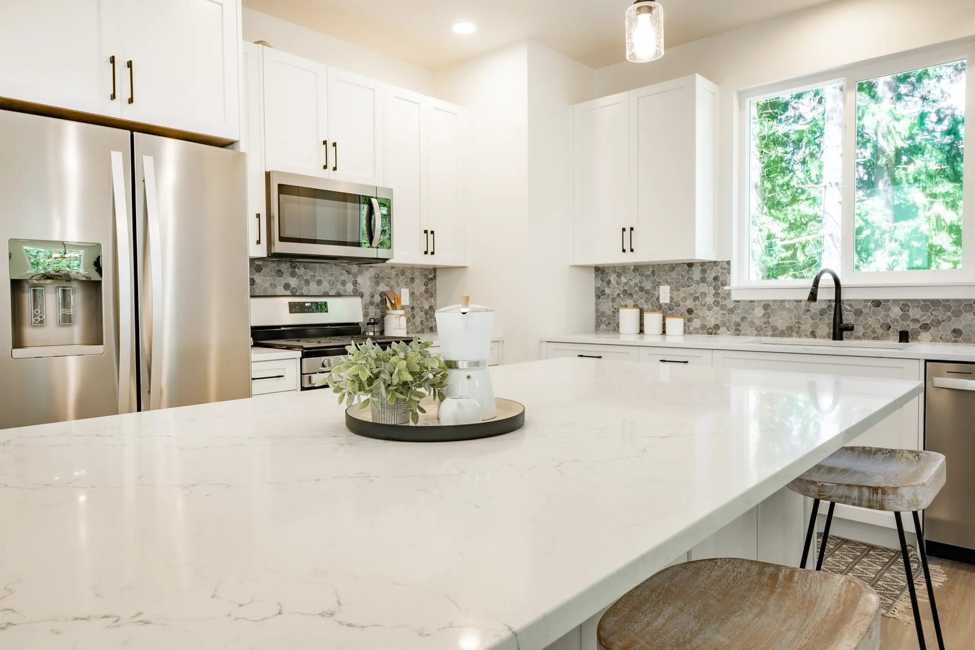 White shaker kitchen with a quartz island, grey hexagon mosaic backsplash and stainless appliances