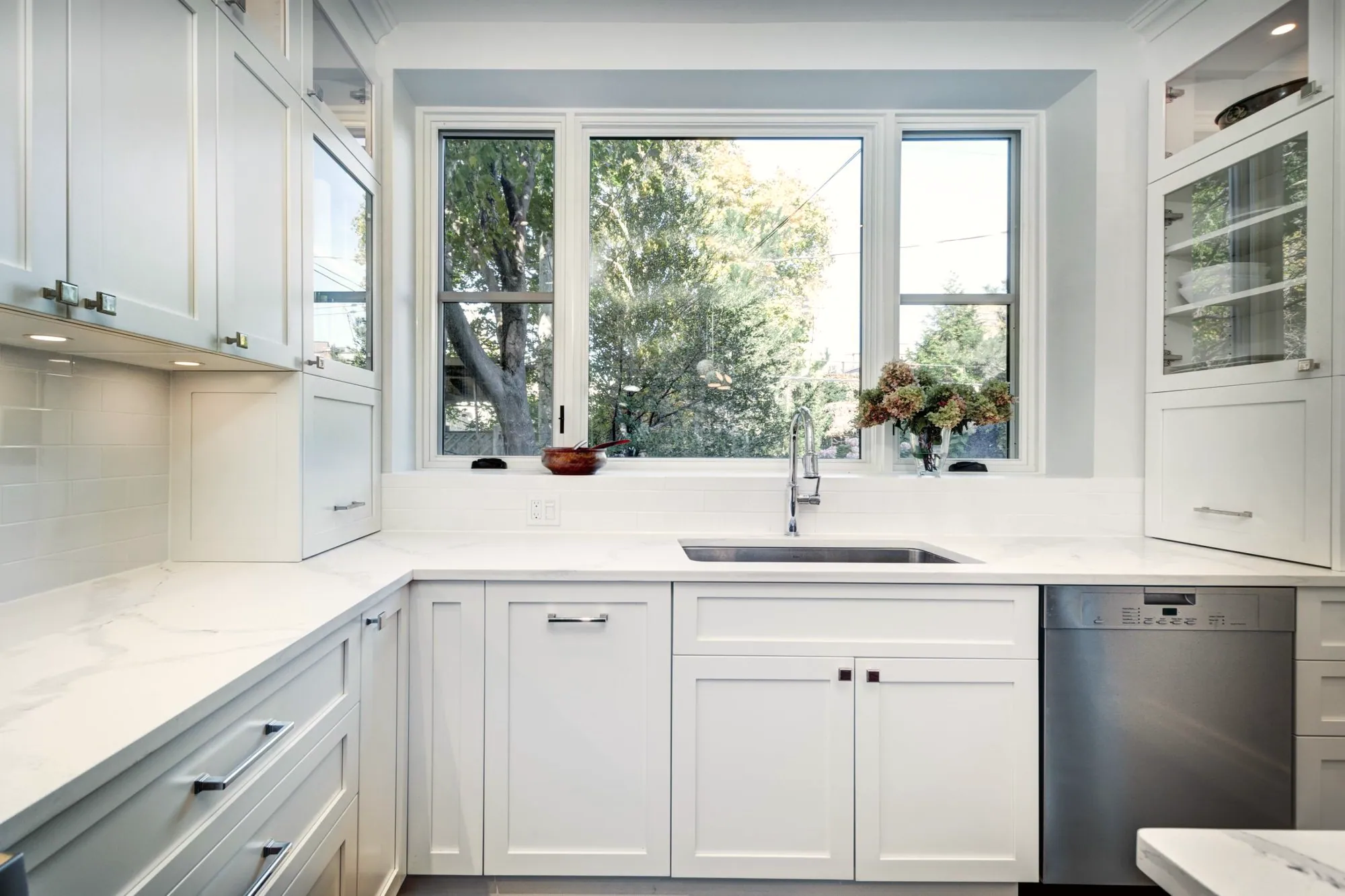 White shaker kitchen with an undermount sink under a wide window and quartz counters