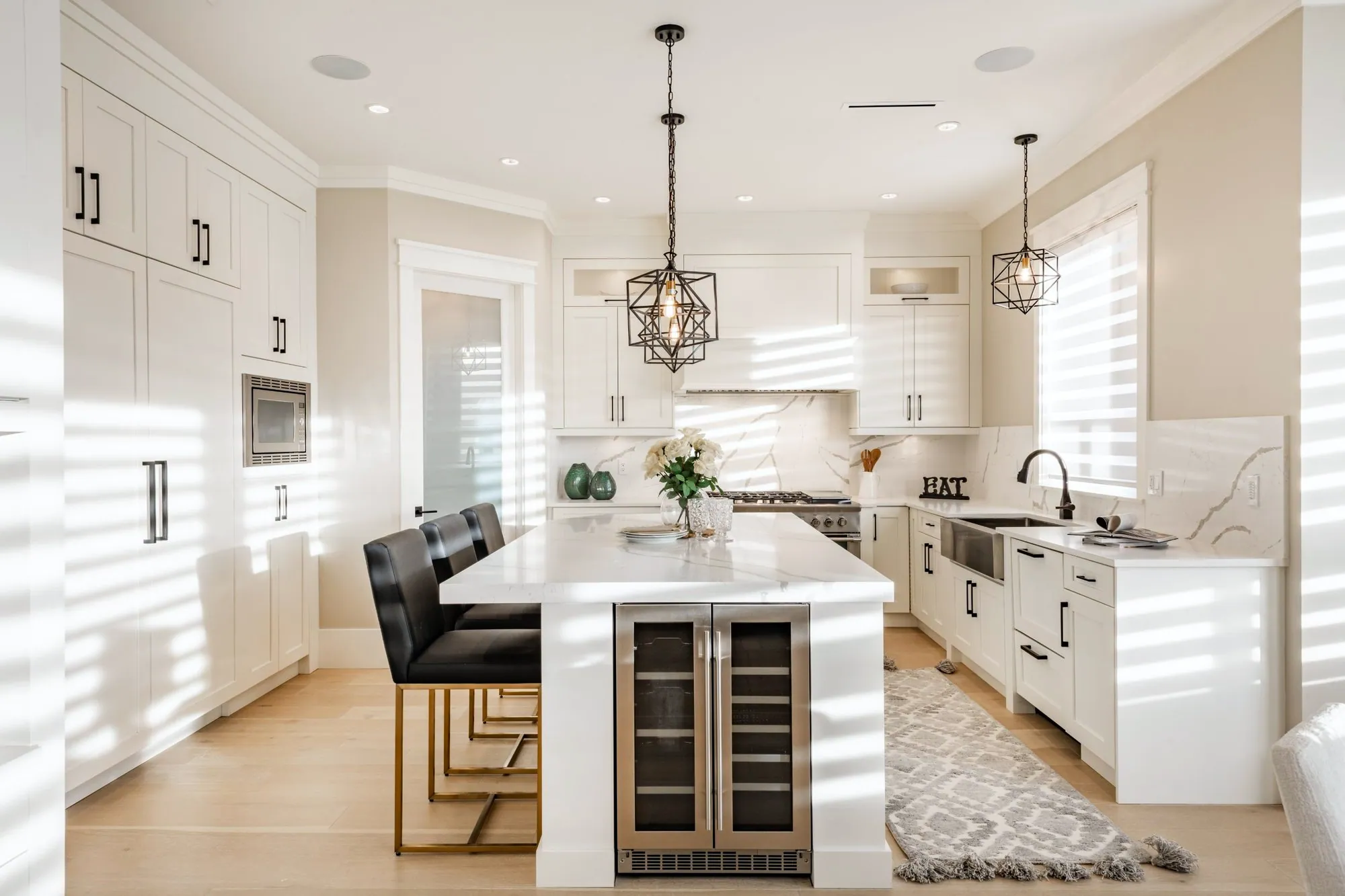 White shaker kitchen with a veined quartz island, geometric black pendants and a full-height quartz backsplash