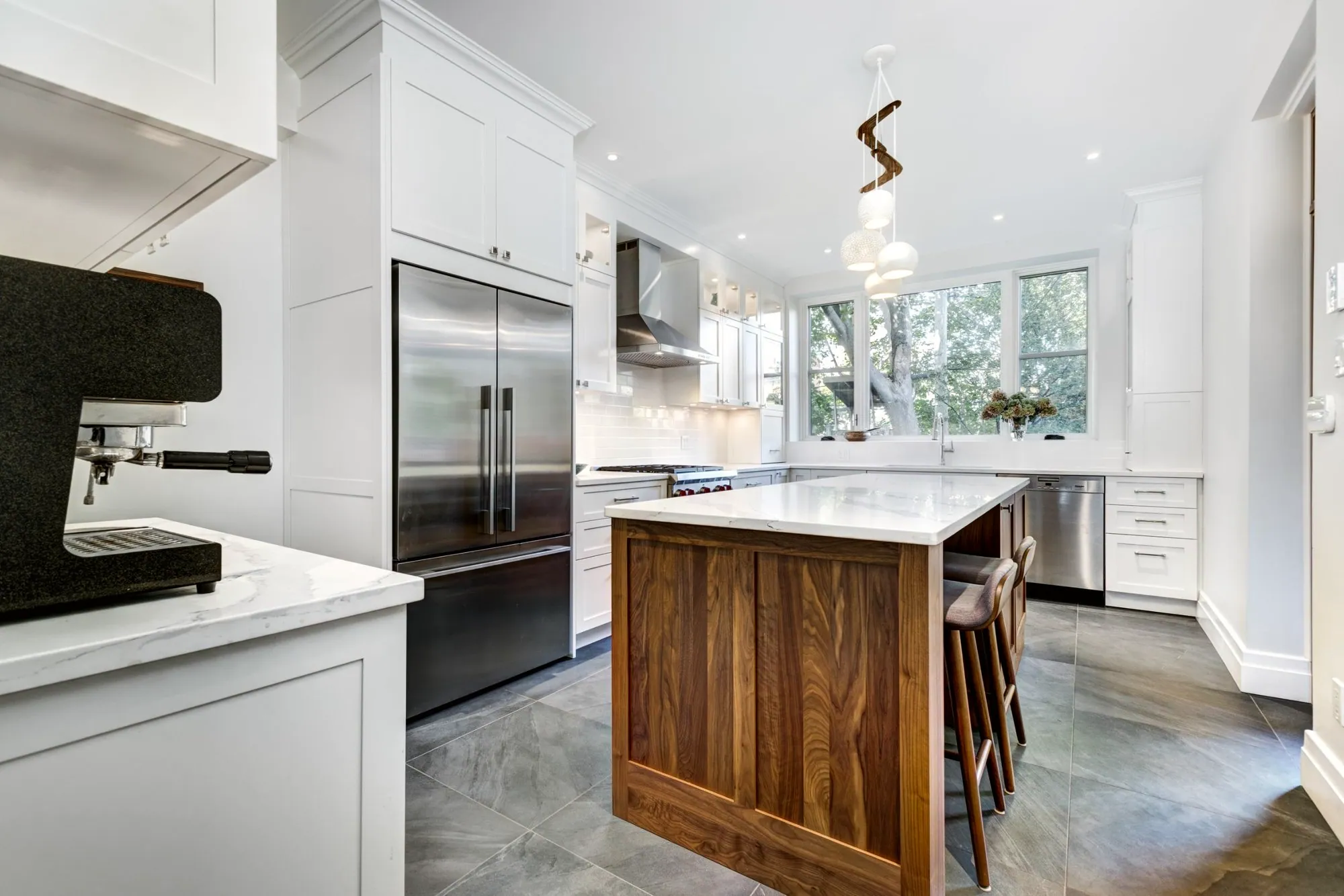 White shaker kitchen with a walnut island, grey stone-look floor tile and a stainless hood